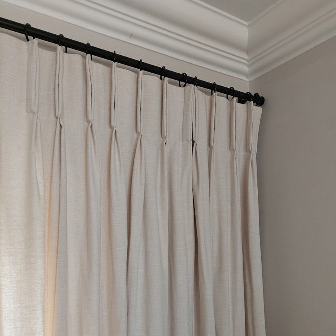 Close-up detail of cream textured linen curtains with a classic pinch pleat heading, installed on a matte black architectural rod by edge.ids in a Johannesburg home.