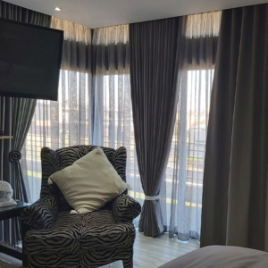 Sophisticated layered window treatments featuring floor-to-ceiling sheers and charcoal drapes by edge.ids, styled with a bespoke upholstered wingback chair.