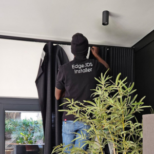 A professional Edge.IDS installer fitting bespoke black wave-fold curtains in a modern residential interior, demonstrating the full implementation service.